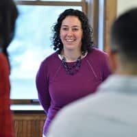 Smiling woman in a purple top speaking to a group