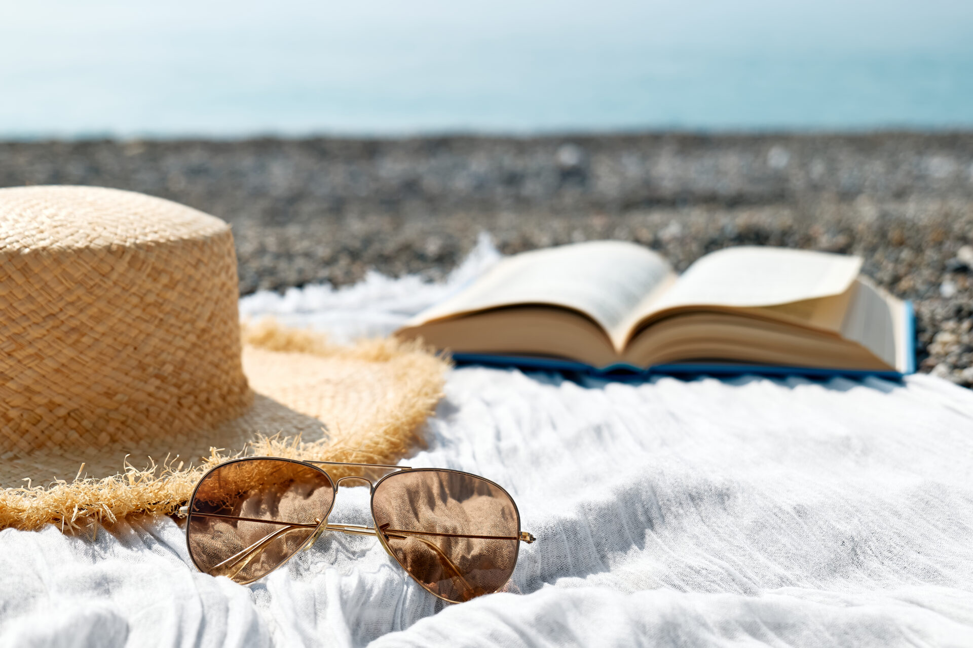 Straw hat, sunglasses and an open book on a towel at a rocky beach