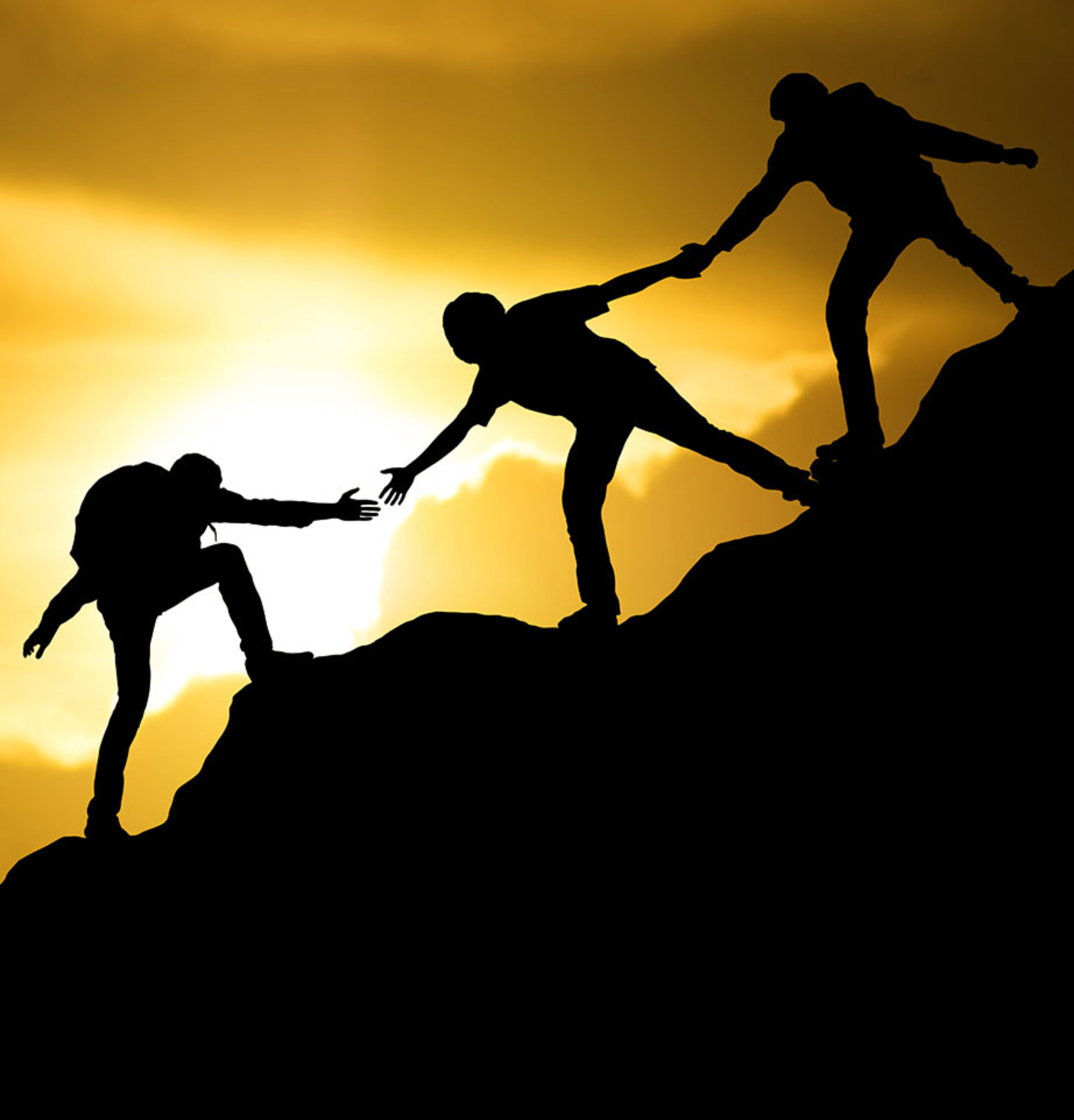 Three people helping each other climb to a mountain peak at sunset