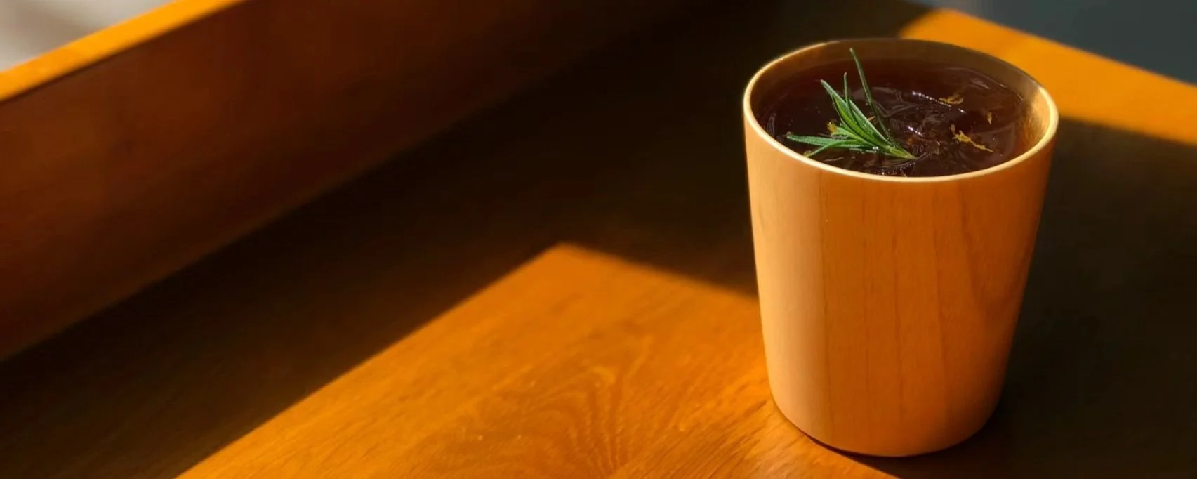 Amber afternoon light on an iced coffee in a wooden cup with rosemary at Square Coffee