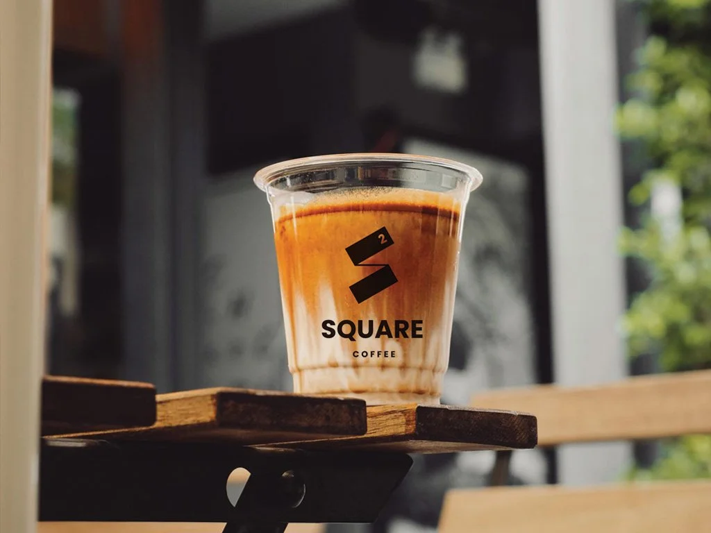 Square Coffee cold latte in a branded cup on an outdoor wooden table in sunlight