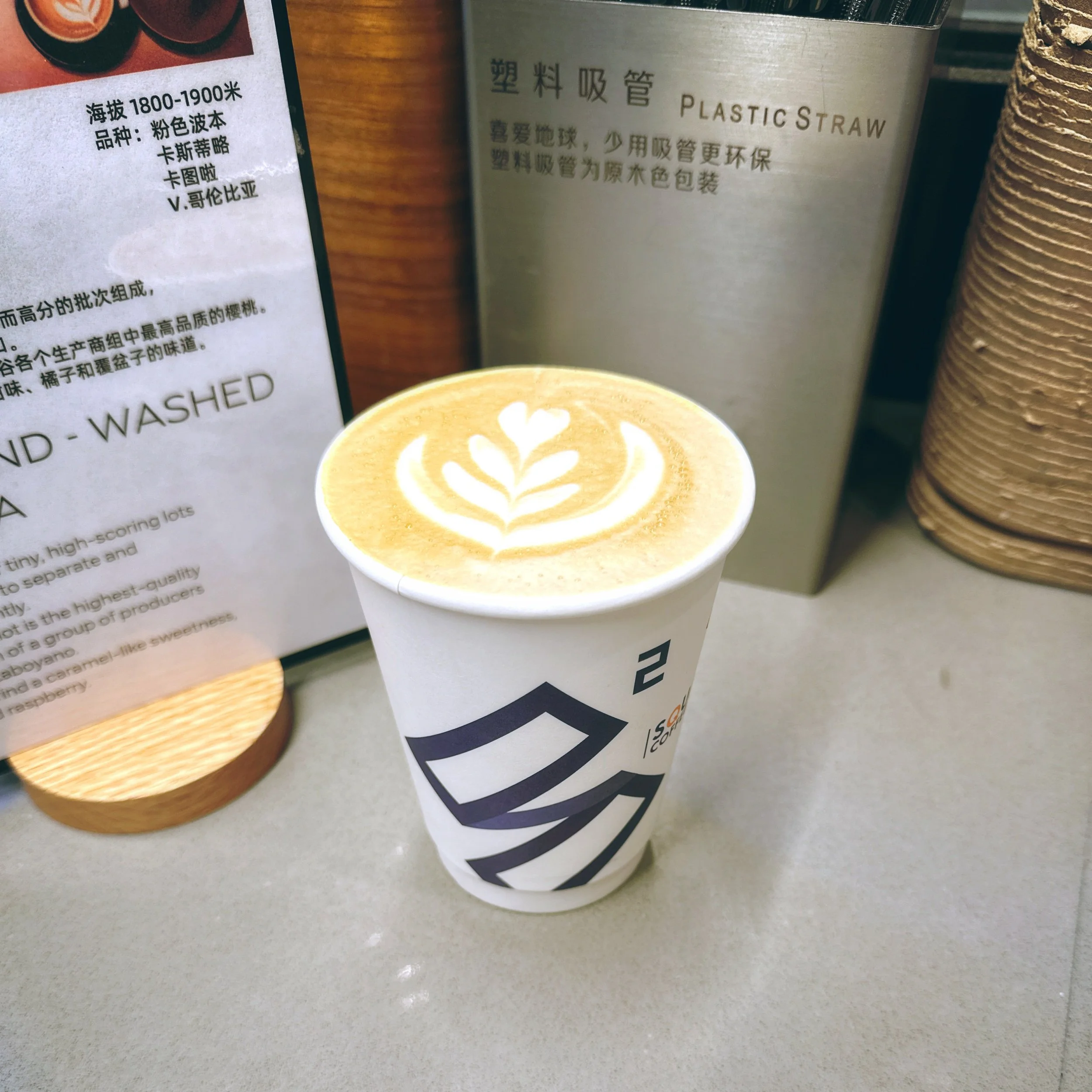 Hot latte with leaf latte art in a Square Coffee branded paper cup