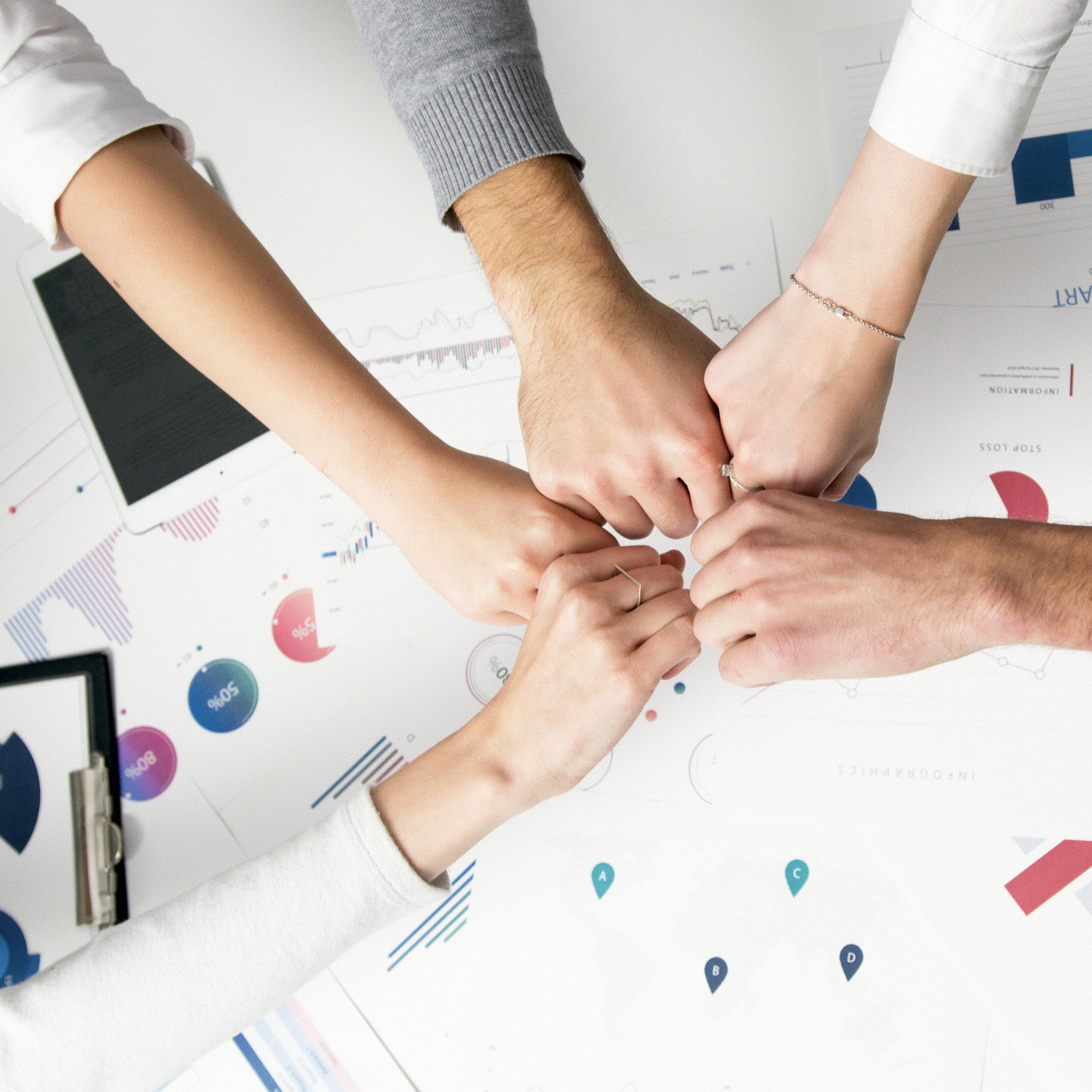 Four people fist-bumping over a table of business charts and infographics
