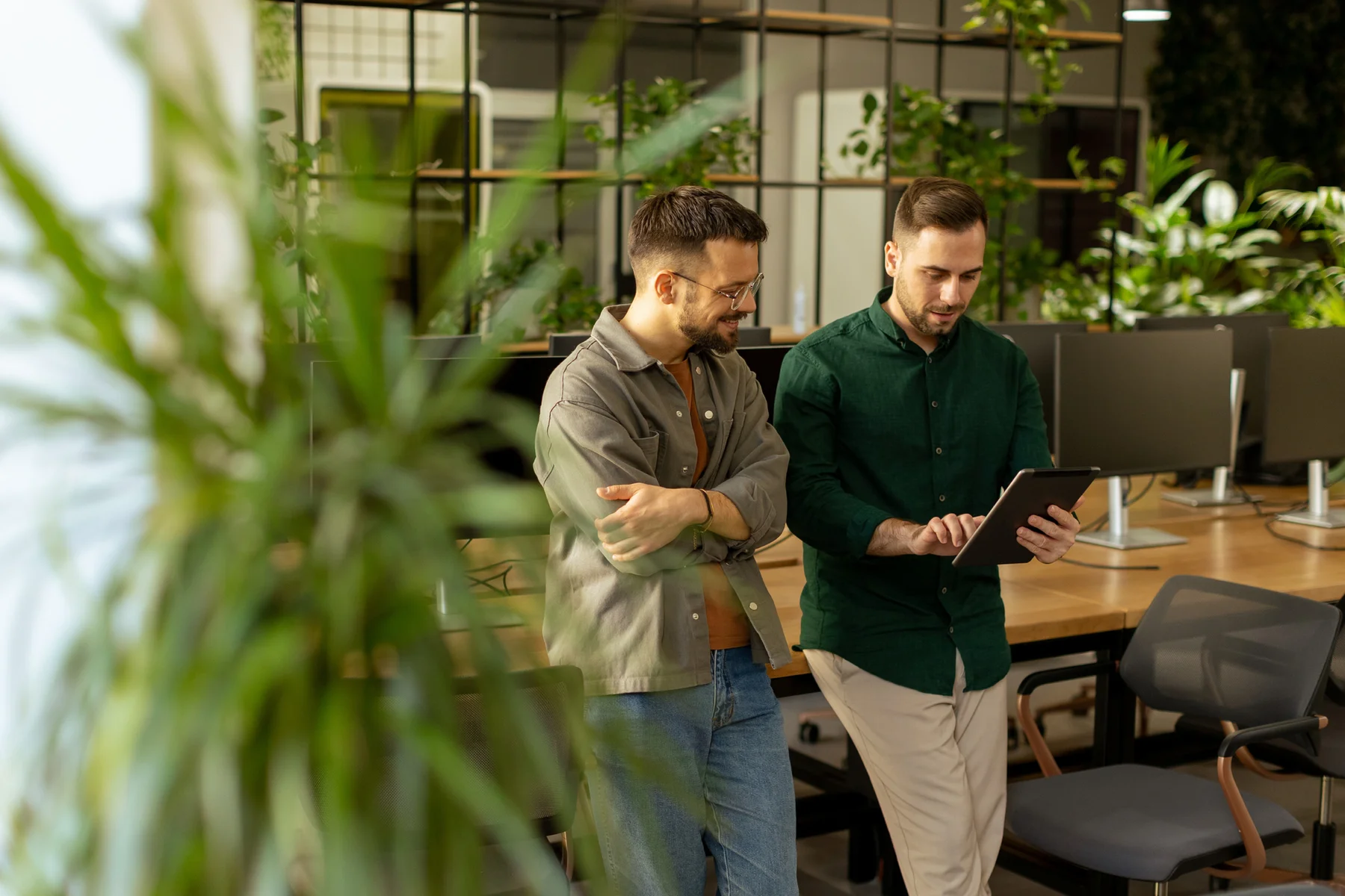 Two colleagues reviewing a tablet in a plant-filled modern office