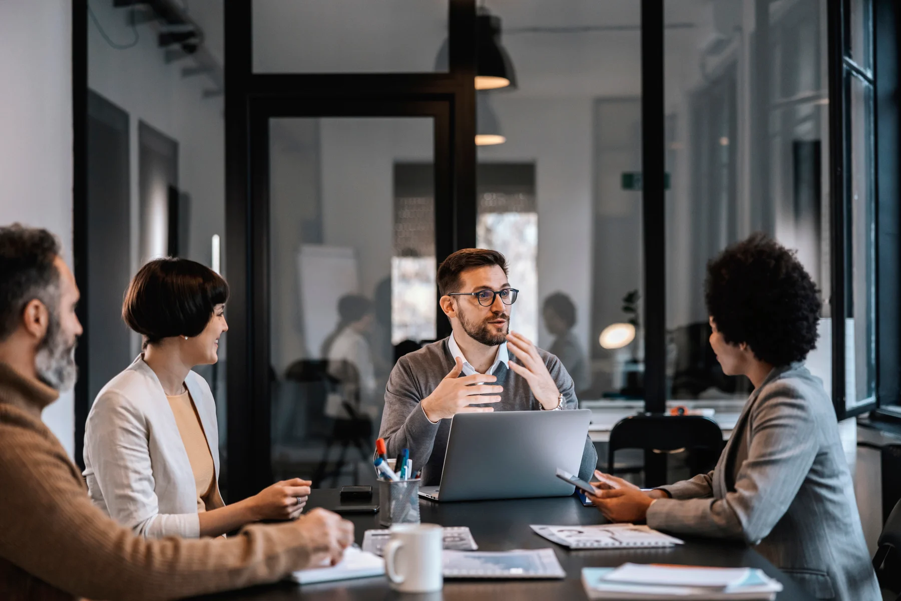 Four professionals in a meeting room, one speaking at the conference table