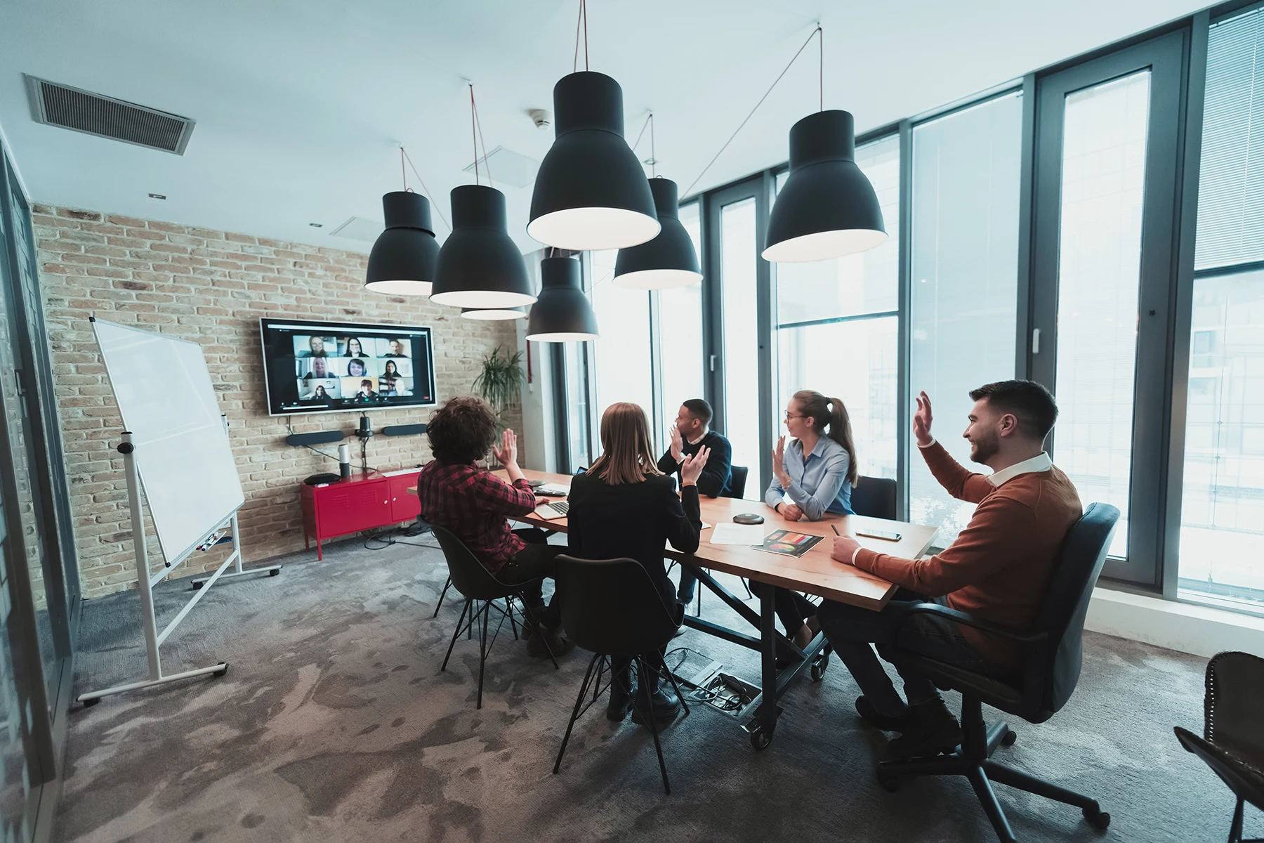 A team in a modern conference room greeting colleagues on a video call
