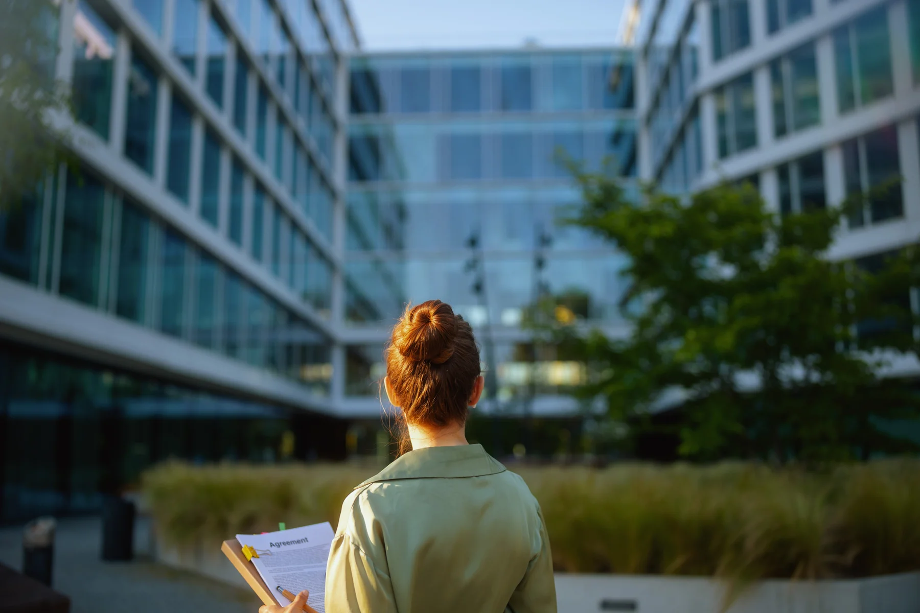 A woman holding documents facing a glass office building complex