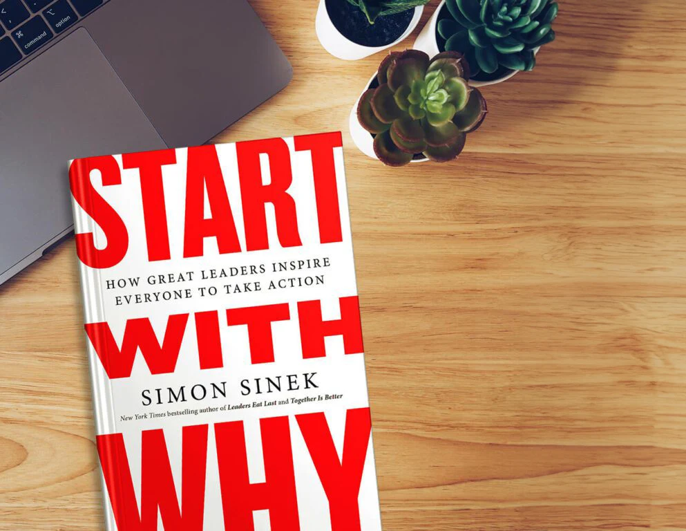 Start With Why by Simon Sinek lying on a wooden desk