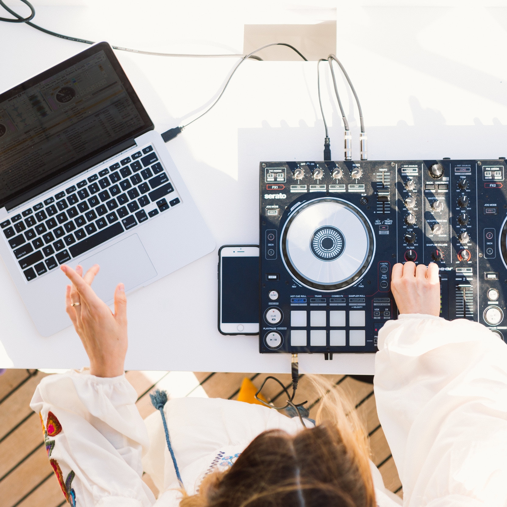 Overhead shot of a female DJ operating a Pioneer and Serato controller and laptop at an outdoor event