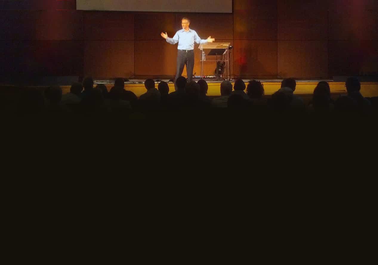 Dr. Brian Wade speaking on stage to a full auditorium