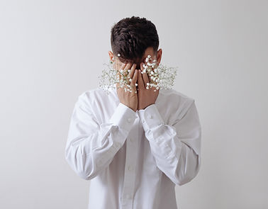 A person in a white shirt covering their face with small white flowers, conveying stress.