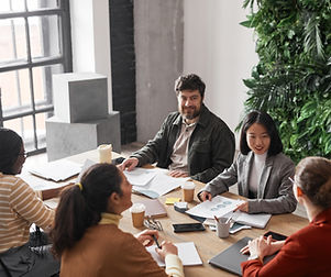 Diverse professionals in a business meeting around a table with a green plant wall behind them.