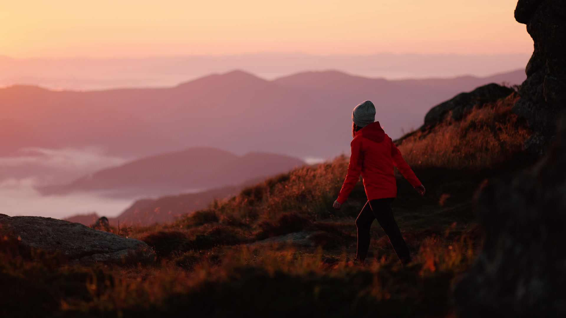 A hiker climbing a mountain ridge at sunrise above misty mountain ranges