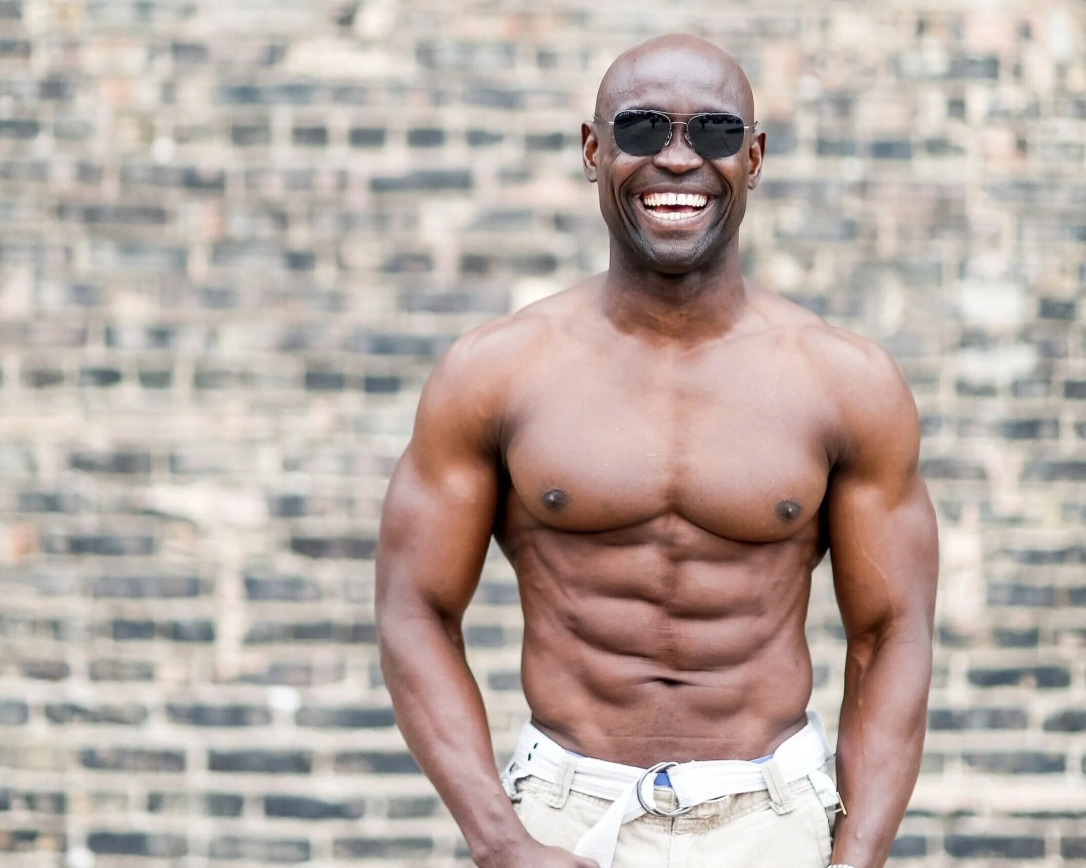 Sunny Akhigbe in sunglasses smiling in front of a brick wall