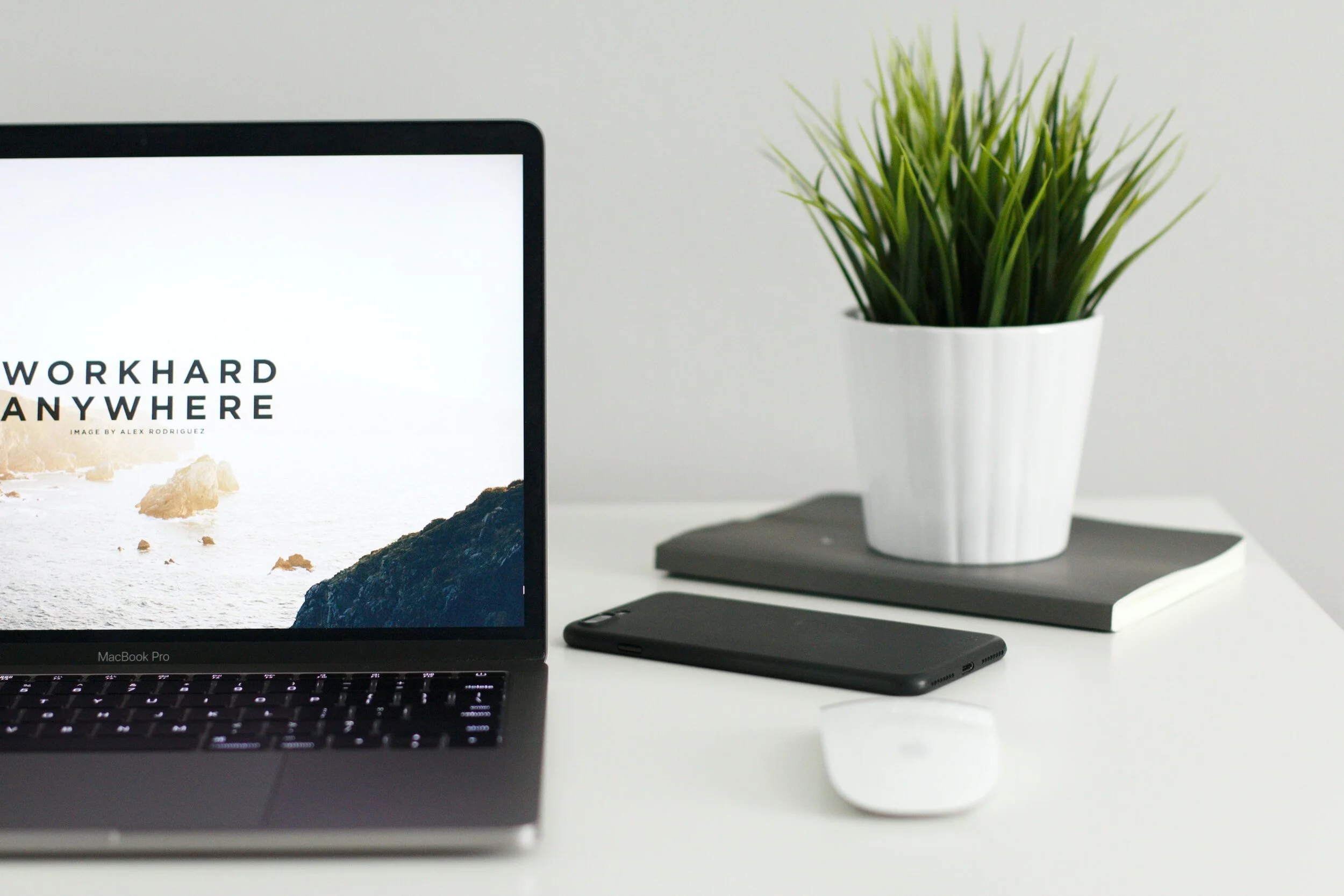Open laptop on a white desk beside a plant and a phone