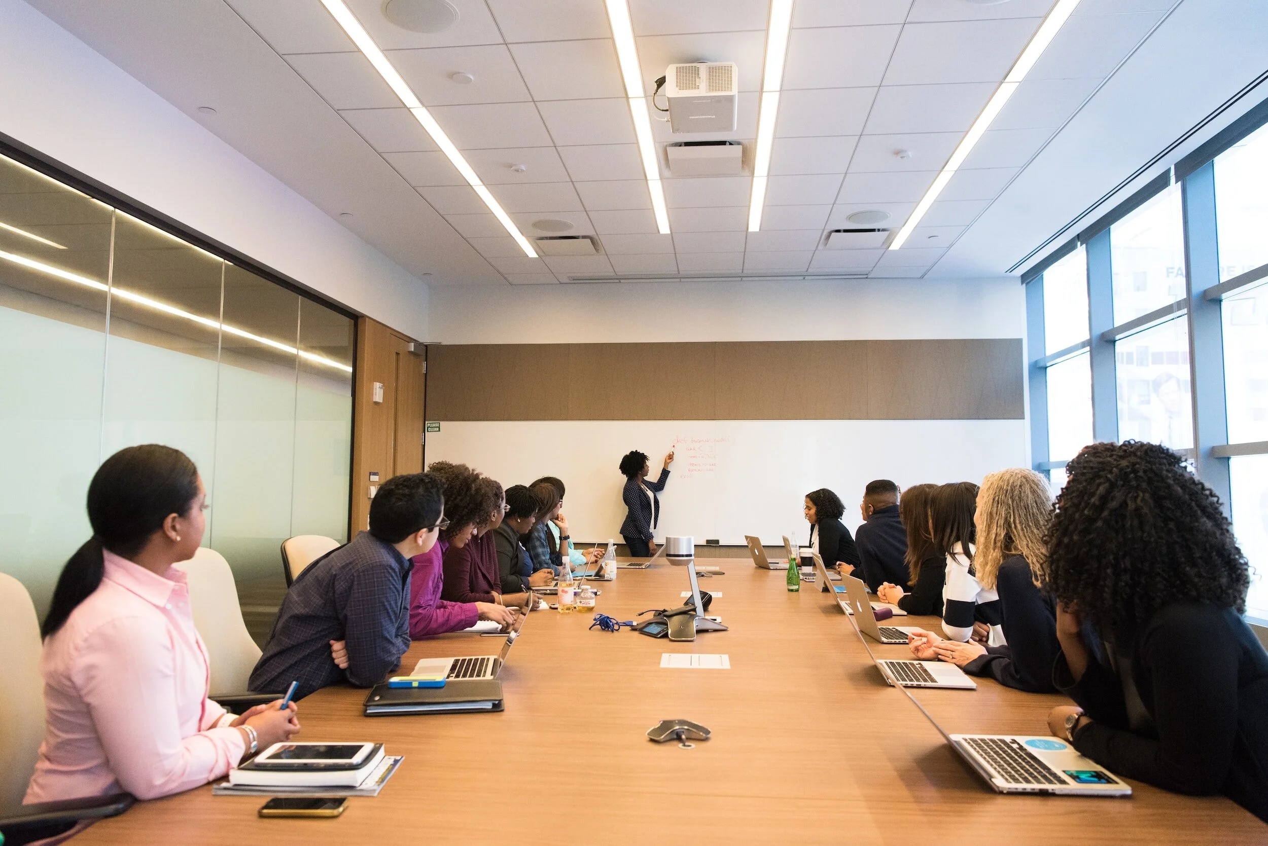 Professionals seated around a long conference table during a leadership workshop while a presenter writes on a whiteboard