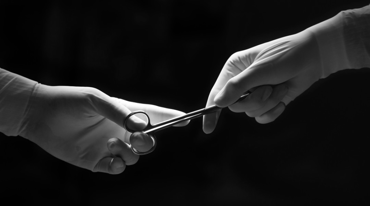 Black-and-white close-up of two gloved surgical hands passing scissors in an operating room