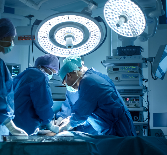 Two surgeons in blue scrubs operating under large operating-room lights