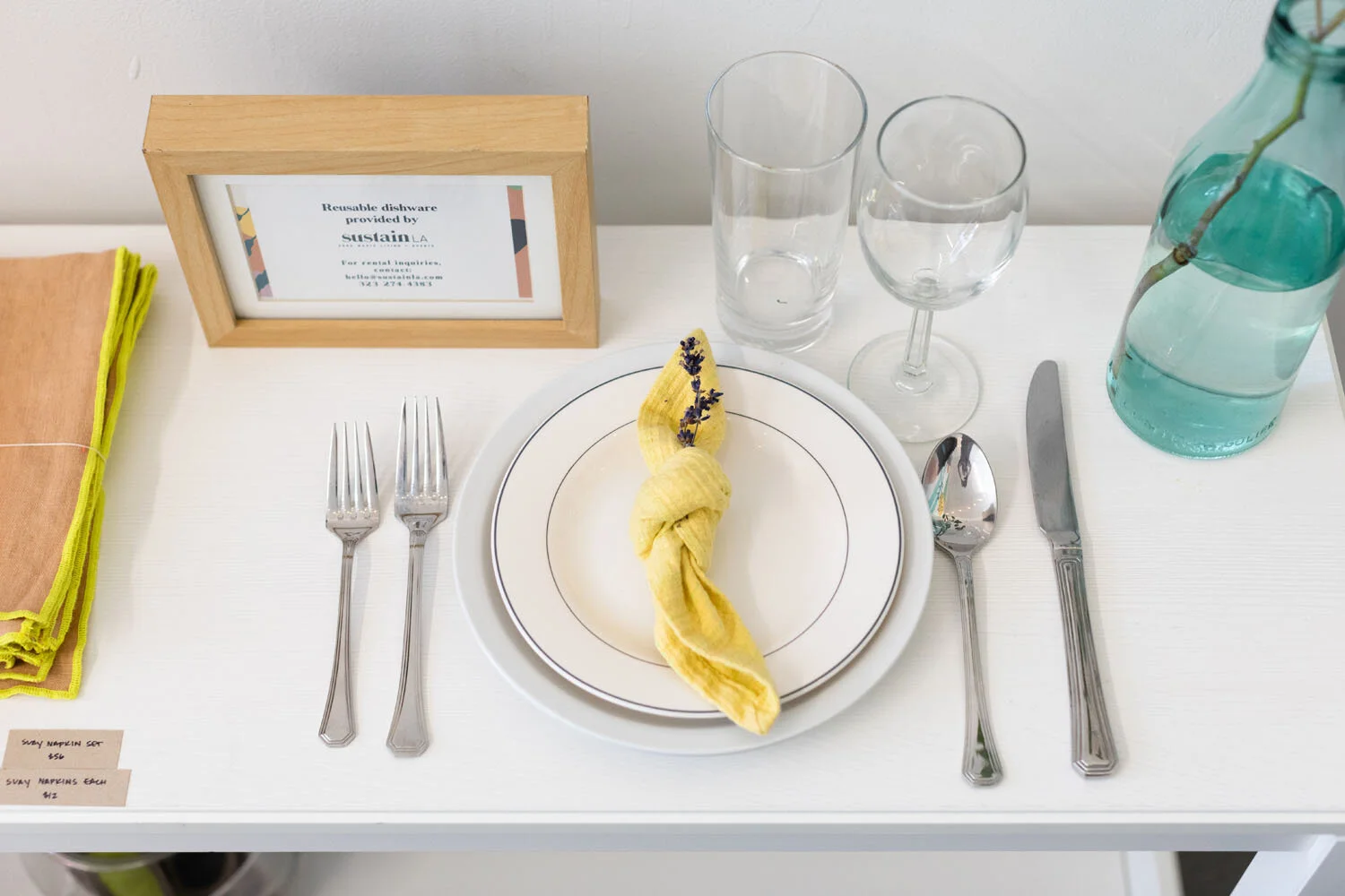 Styled place setting with plate, cutlery, yellow linen napkin, glasses and Sustain LA reusable dishware card
