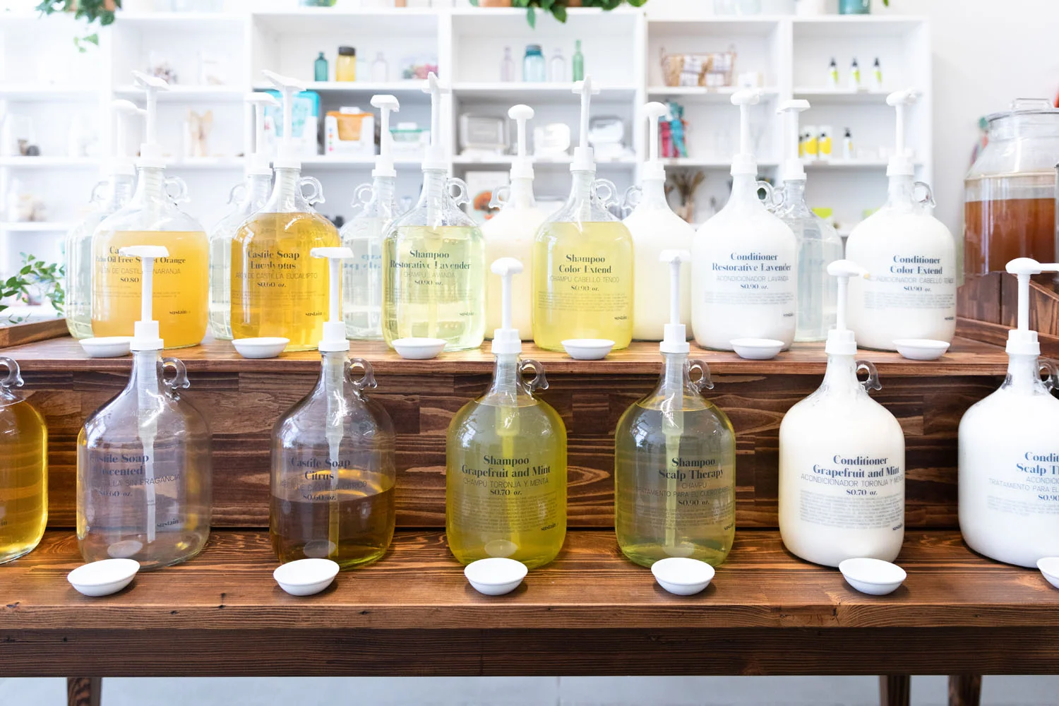 Rows of large glass jugs of shampoo, conditioner and castile soap on the Sustain LA refill station shelving