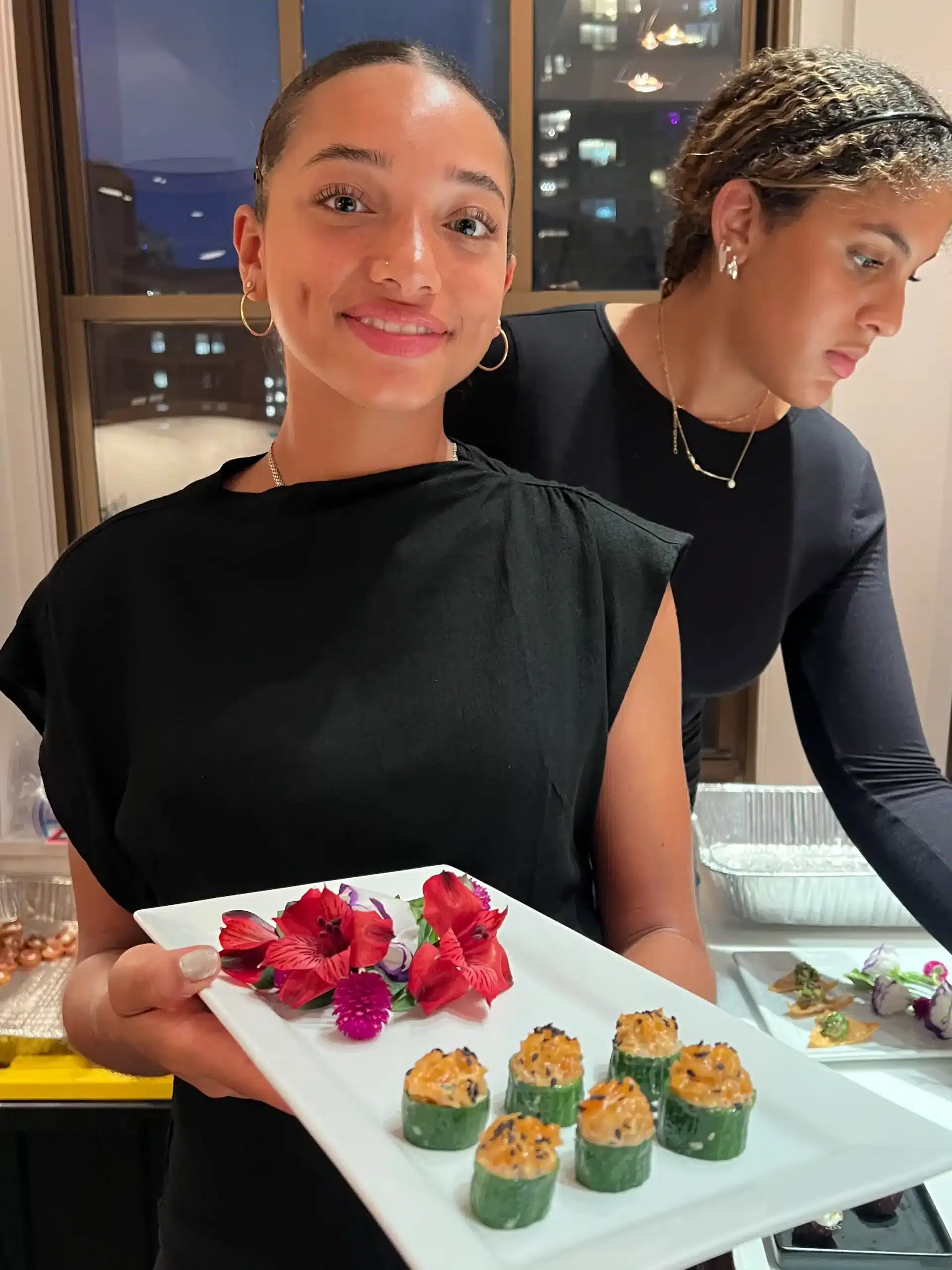 Two Sweet Basil servers presenting a tray of stuffed cucumber canapés at a night-time New York event