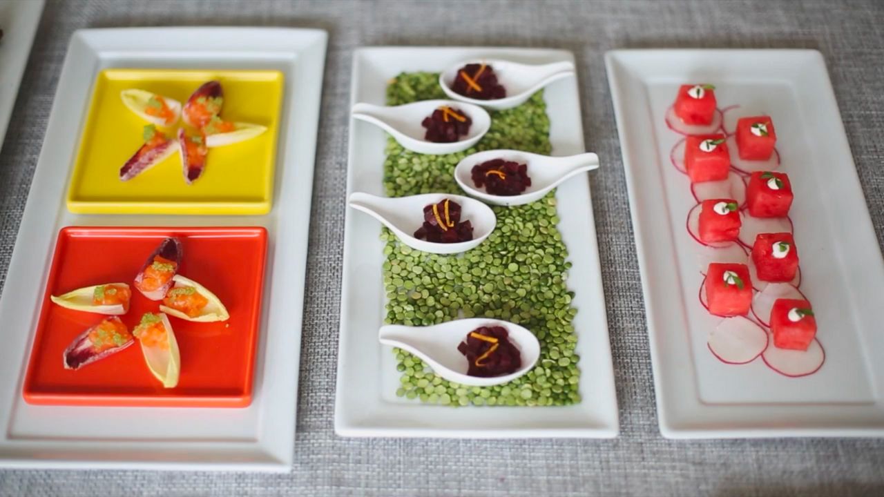 Colorful passed hors d'oeuvres — endive canapés, spoons of tartare on green peas and watermelon bites — arranged on white platters