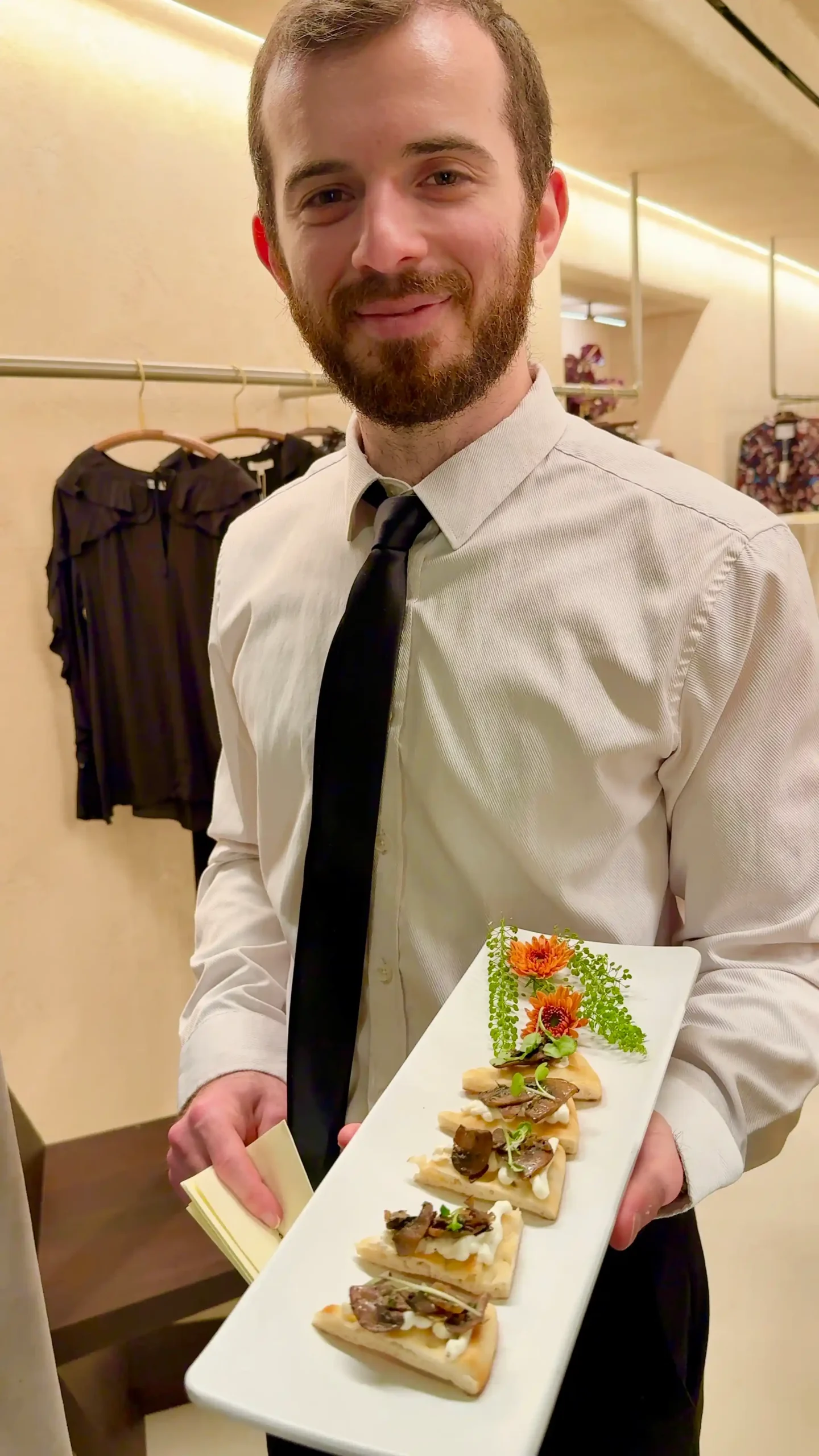 Sweet Basil server in a white shirt and black tie presenting a long white platter of garnished crostini at a boutique private party