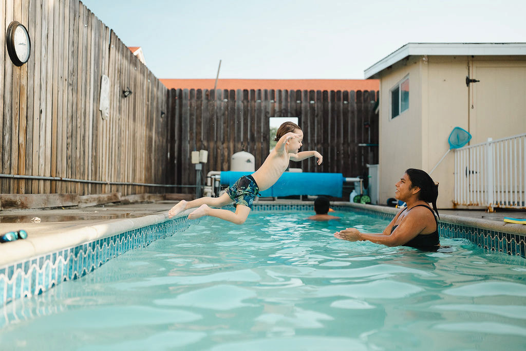 A child jumping into a backyard pool toward a female instructor in the water