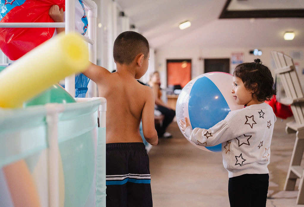 Two young children near colorful pool toys and foam noodles at the indoor facility