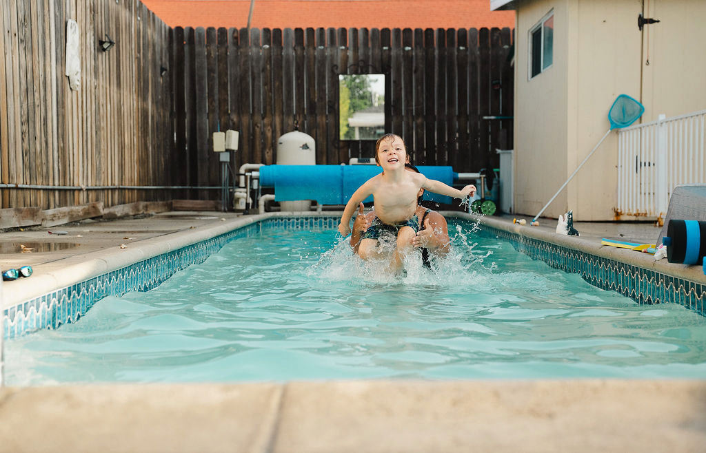 A young boy being lifted out of the water by an instructor, a mid-splash action shot