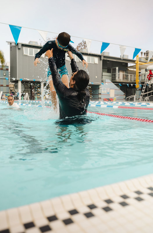 An instructor lifting a young child high out of the water in an outdoor pool