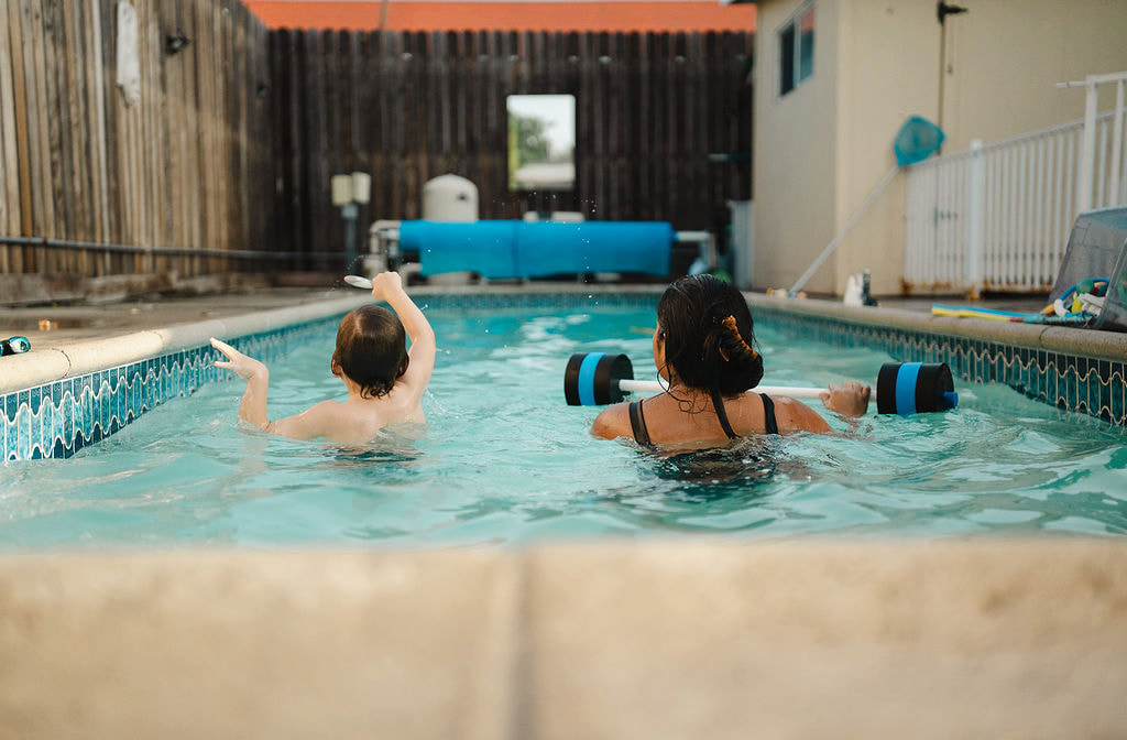 A female instructor and child practicing arm movements in a backyard pool