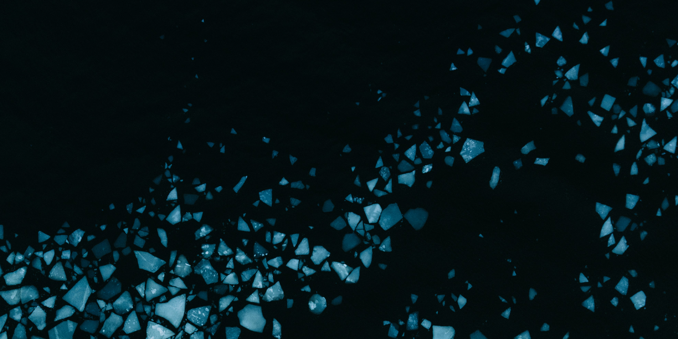 Dark abstract field of scattered glowing blue crystal fragments on black
