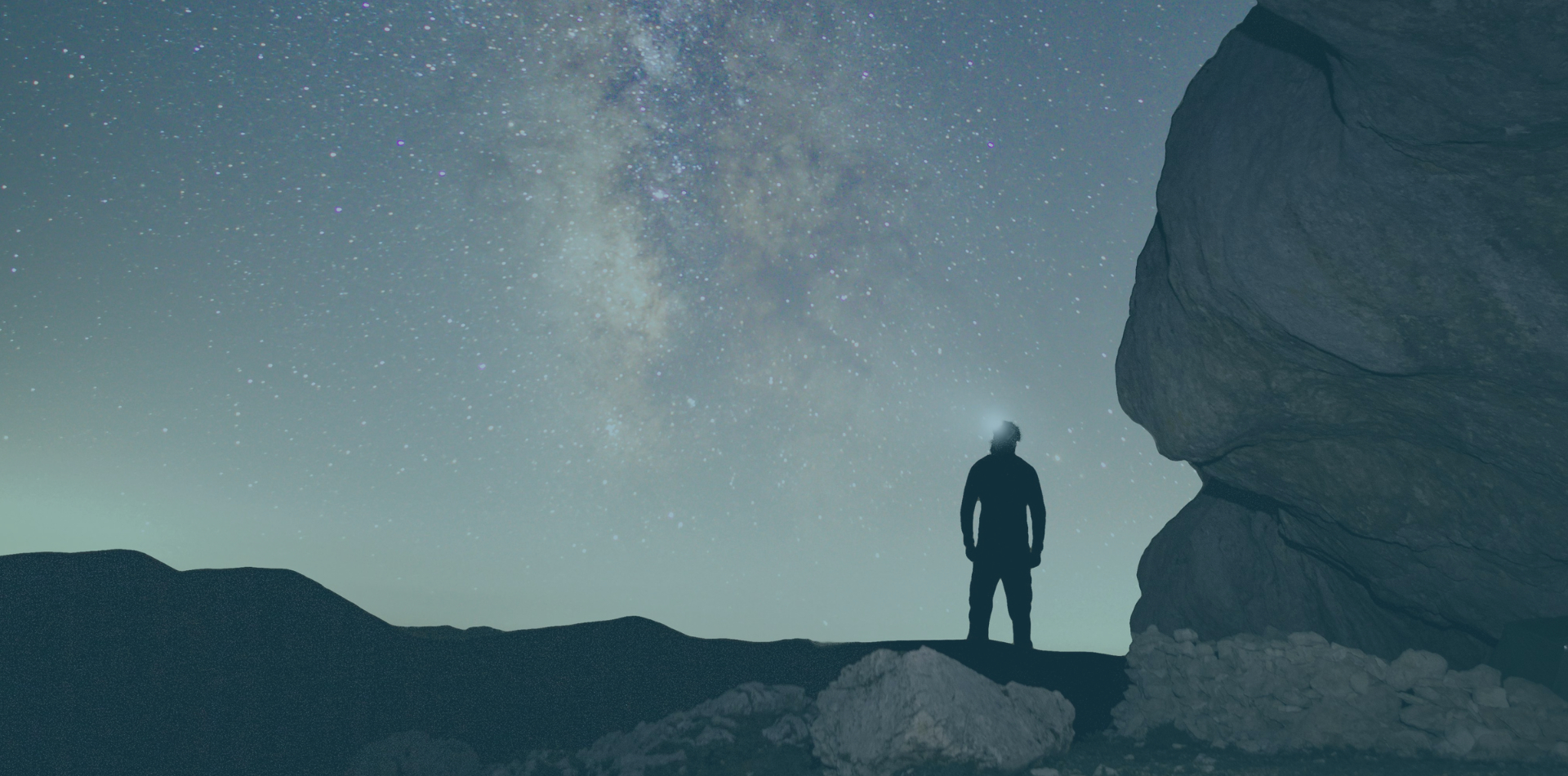 Silhouette of a person gazing at the Milky Way starry night sky beside a large rock formation