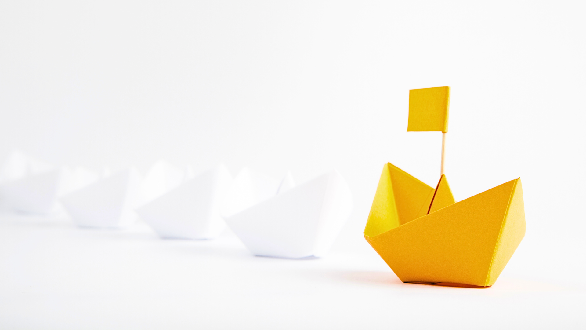 Yellow origami boat leading a fleet of white paper boats