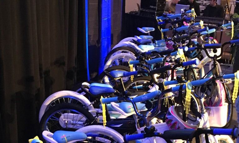 Row of assembled blue children's charity bikes lit with blue lighting at an indoor venue