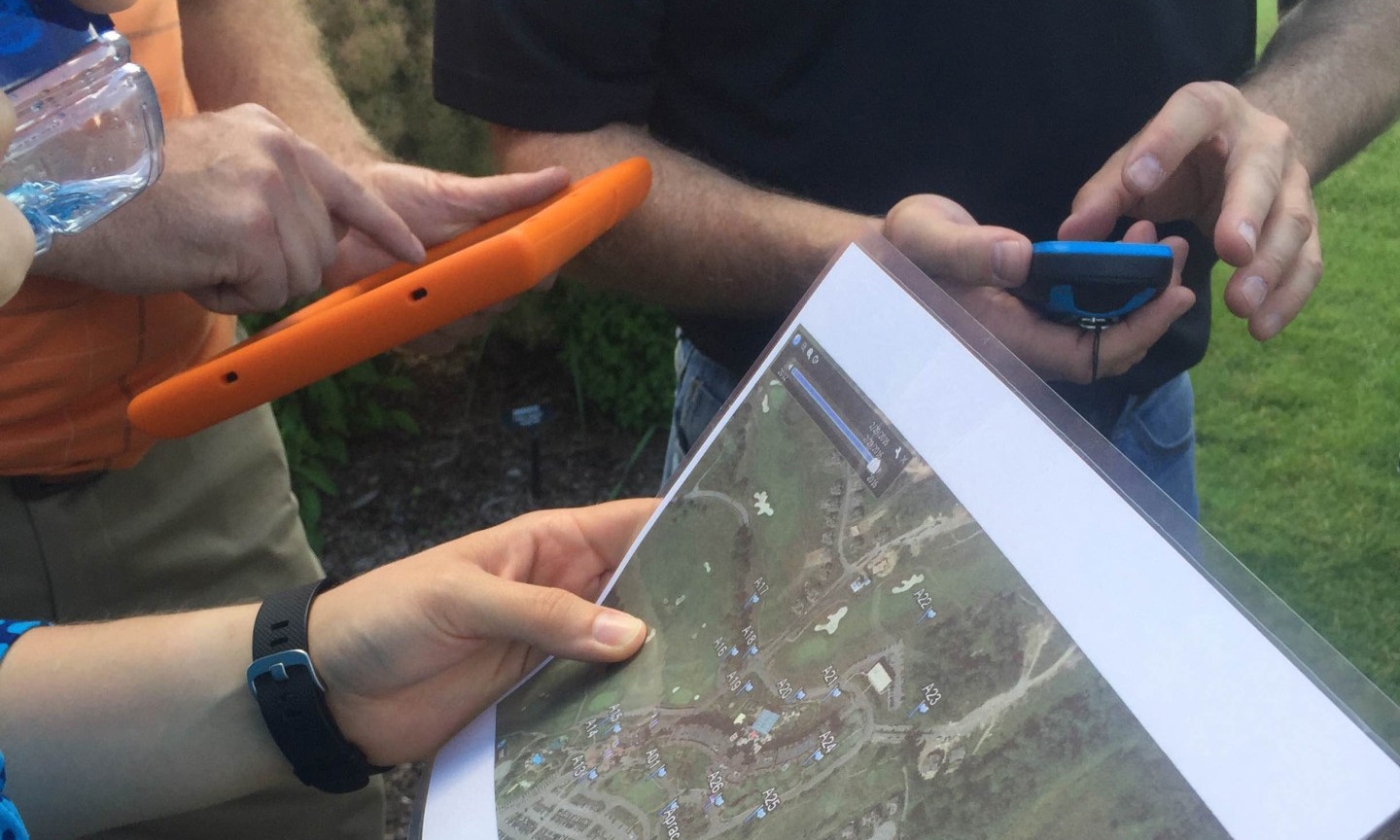 Close-up of participants' hands holding a tablet, GPS device, and printed map during a geo trekking activity