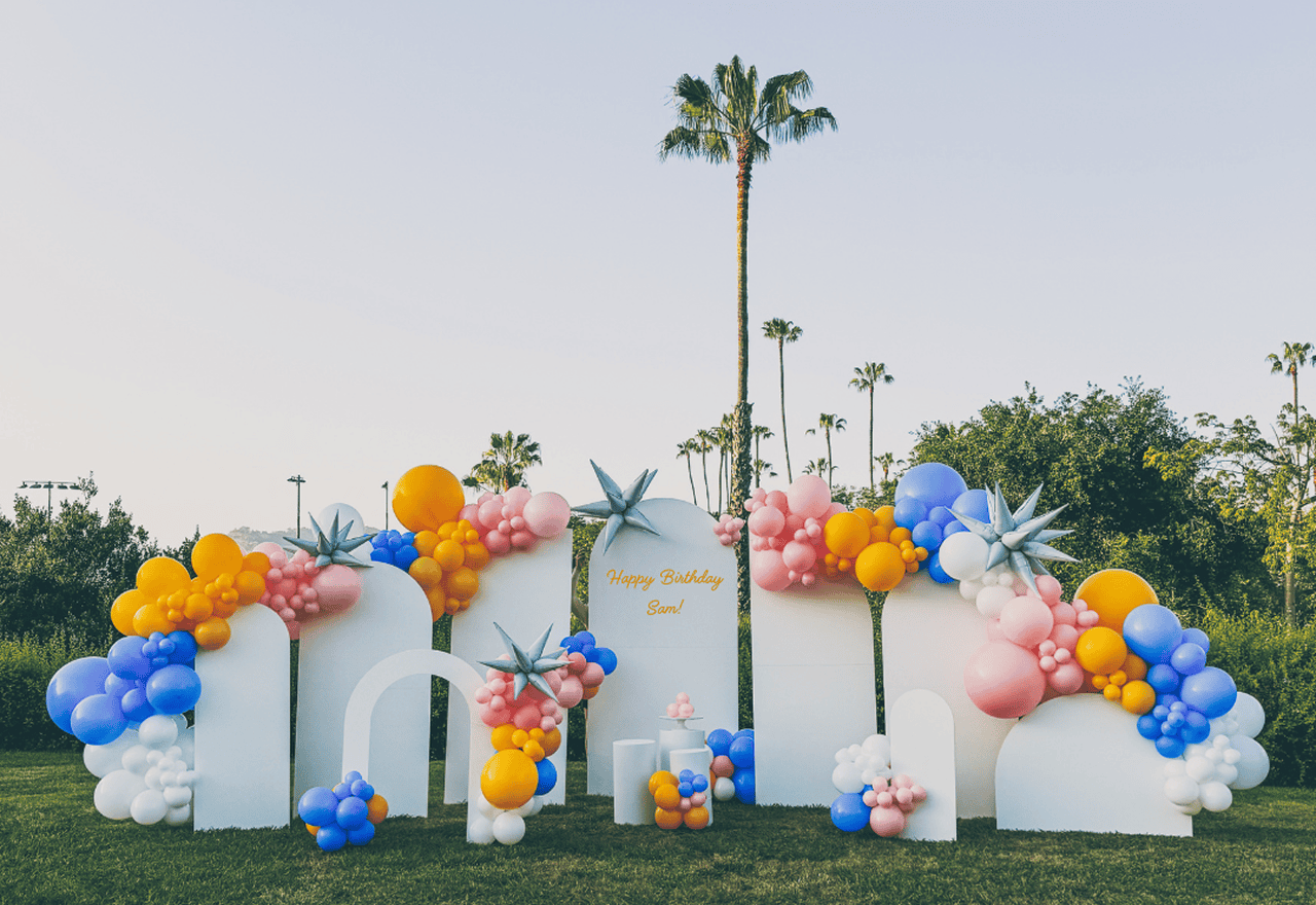 Outdoor birthday setup with white arch panels, colorful garlands and a Happy Birthday Sam sign