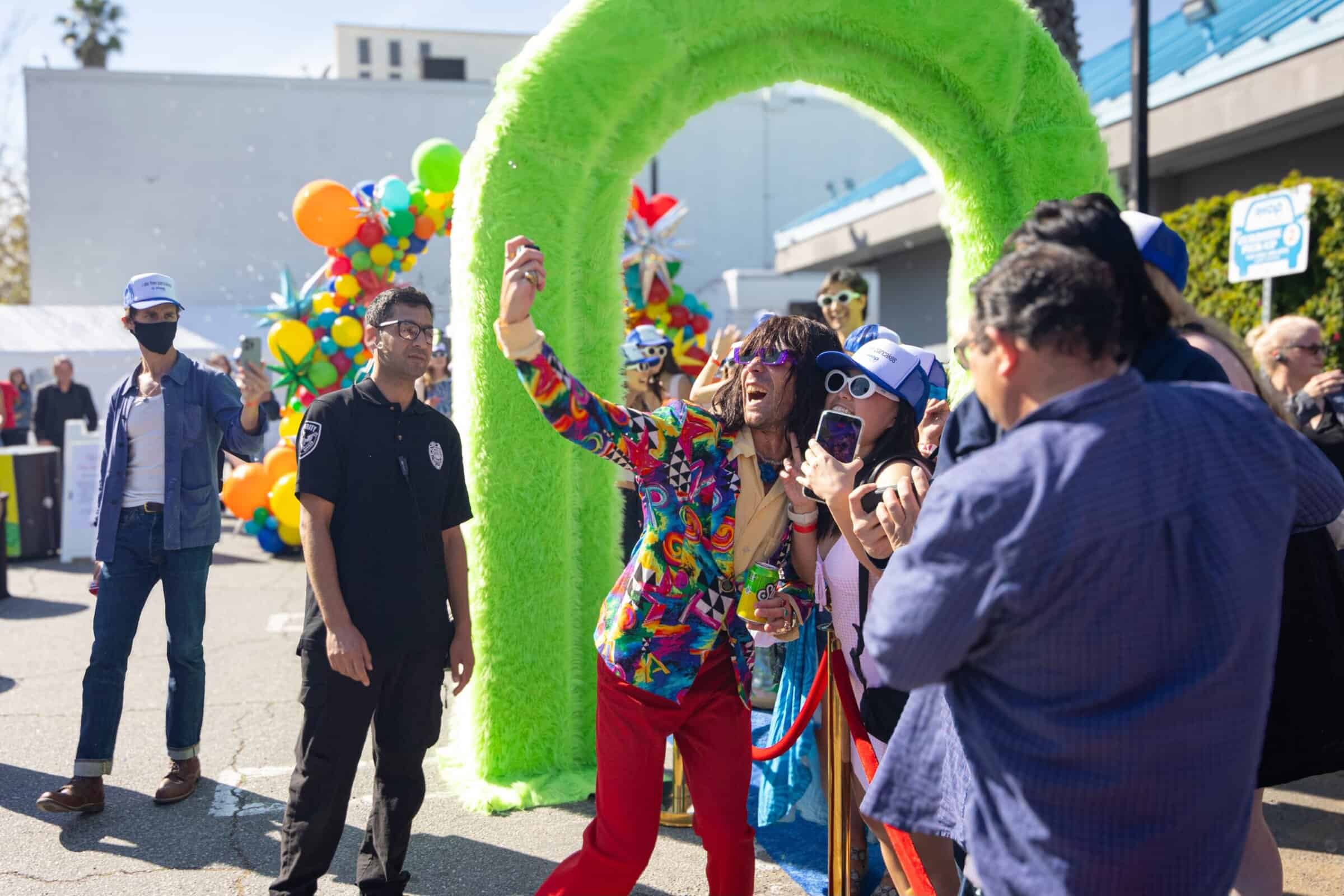 Outdoor IHOP brand activation in Hollywood with a colorful balloon arch and a performer in a rainbow outfit posing with a crowd