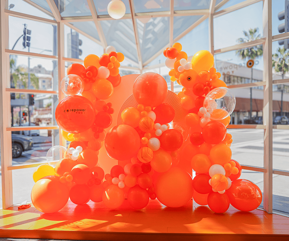 Orange and yellow balloon sculpture inside a glass CorePower Yoga storefront