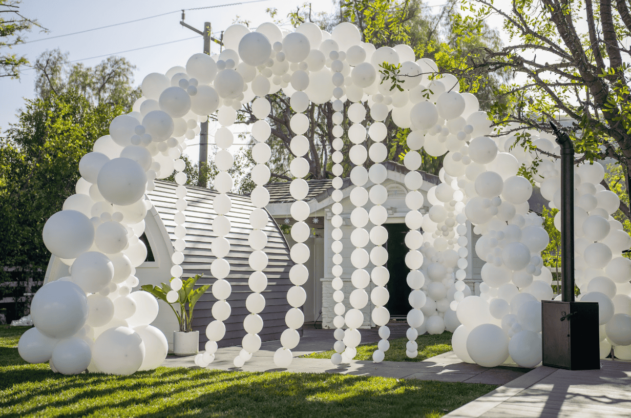 Large all-white balloon arch with hanging balloon strands over a garden shed