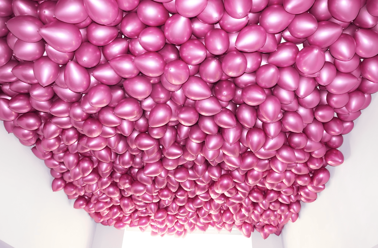 Dense metallic hot-pink balloon ceiling installation filling a room