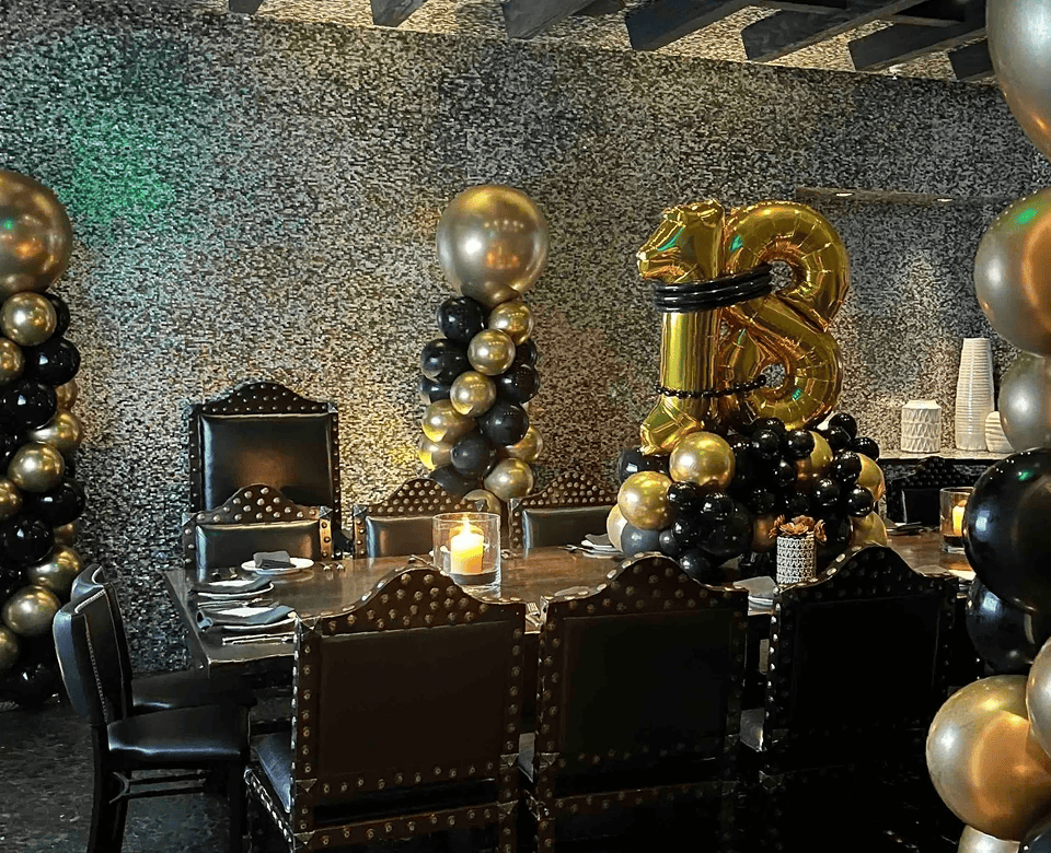 Dark upscale restaurant table with black and gold balloon centerpieces and a number 18 foil balloon