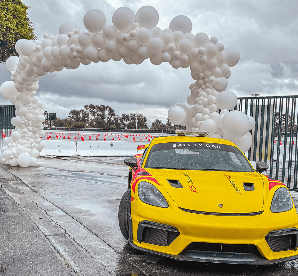 Yellow Porsche safety car under a white organic balloon arch
