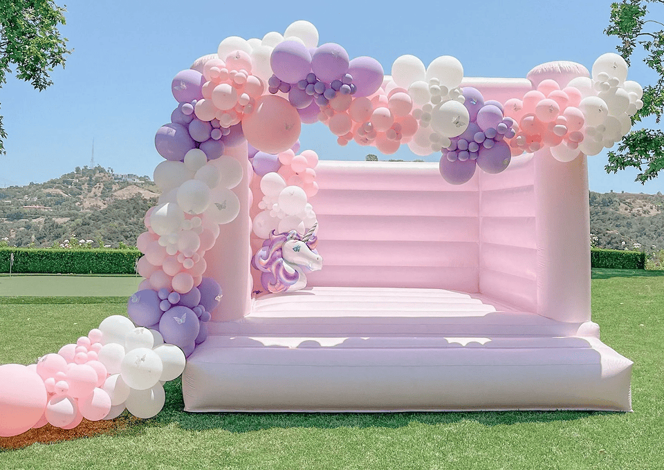 Pink bounce house with a lavender and pink balloon arch and unicorn foil balloon