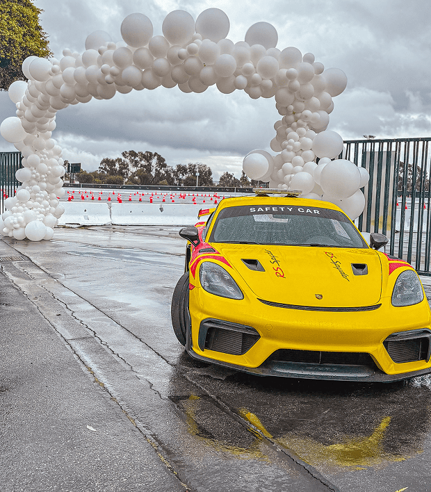 Yellow Porsche safety car under a white organic balloon arch