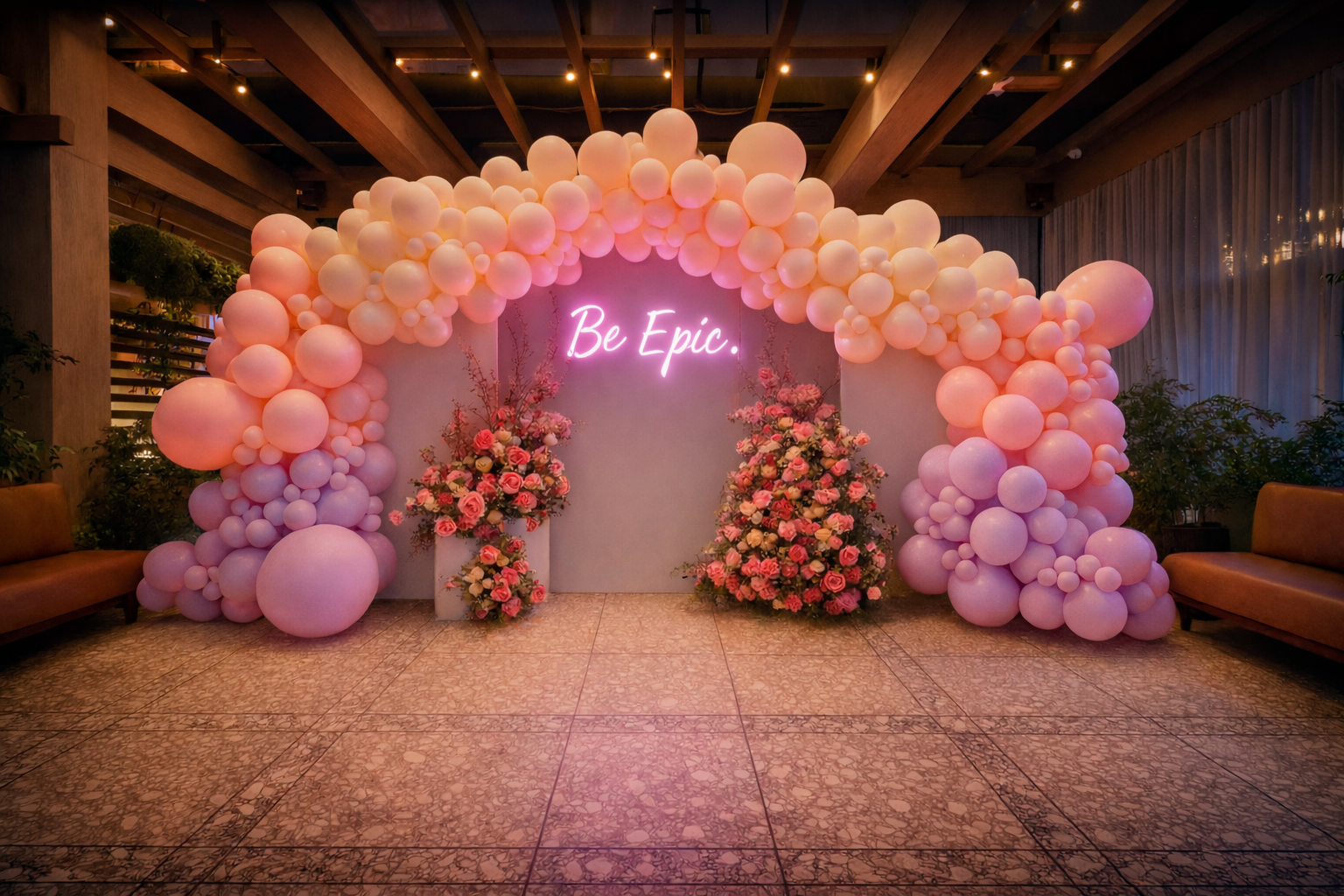 Pink and lavender balloon arch with a "Be Epic." neon sign and floral arrangements in an indoor Los Angeles venue