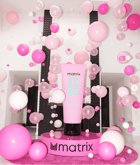 Matrix InstaCure product tube on a pink platform surrounded by floating pink and white balloons