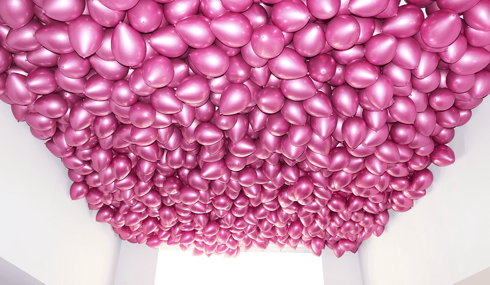 Dense metallic hot-pink balloon ceiling filling a room
