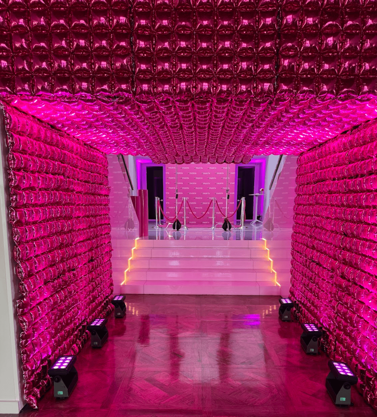 Hot-pink metallic balloon tunnel leading to a lit Matrix stage